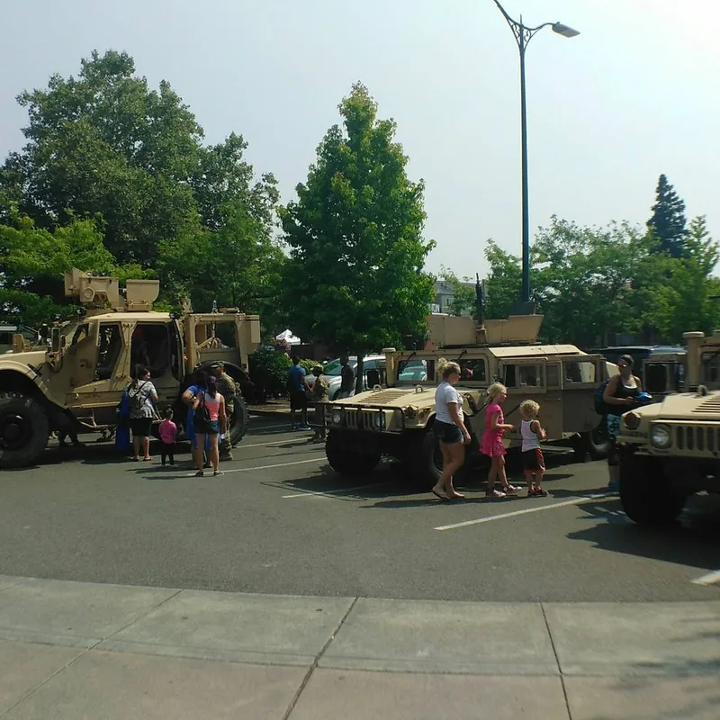Vehicles and visitors gathered at an outdoor display beneath trees.